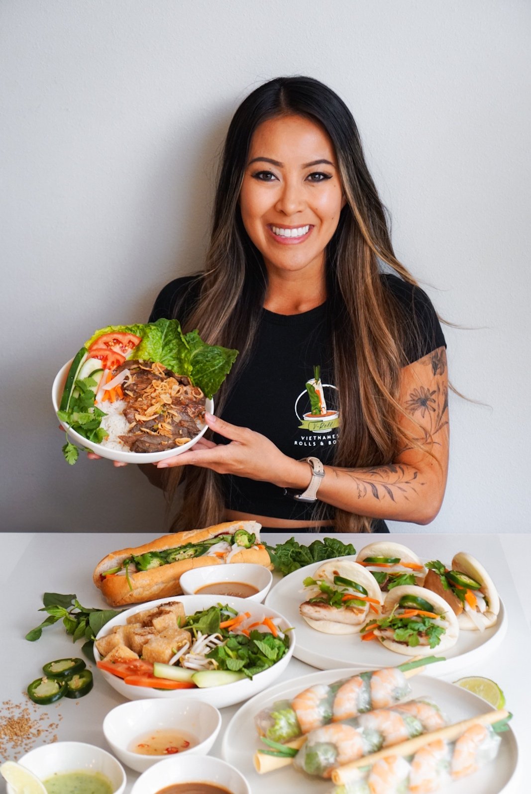 Stephanie Nghiem holding a bowl behind a table of bánh mì, bao and spring rolls