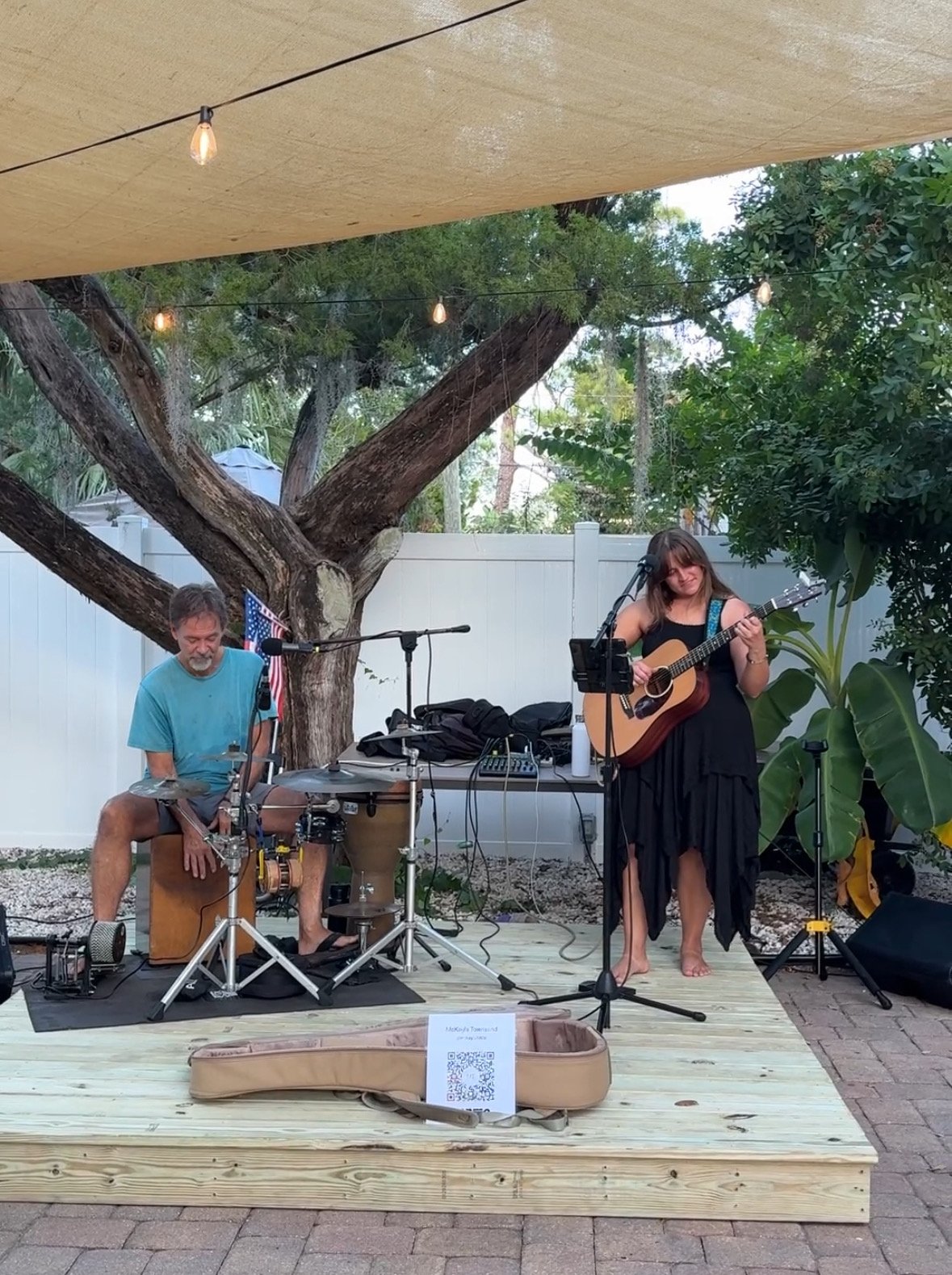 A duo playing guitar and cajón on the patio stage under the oak