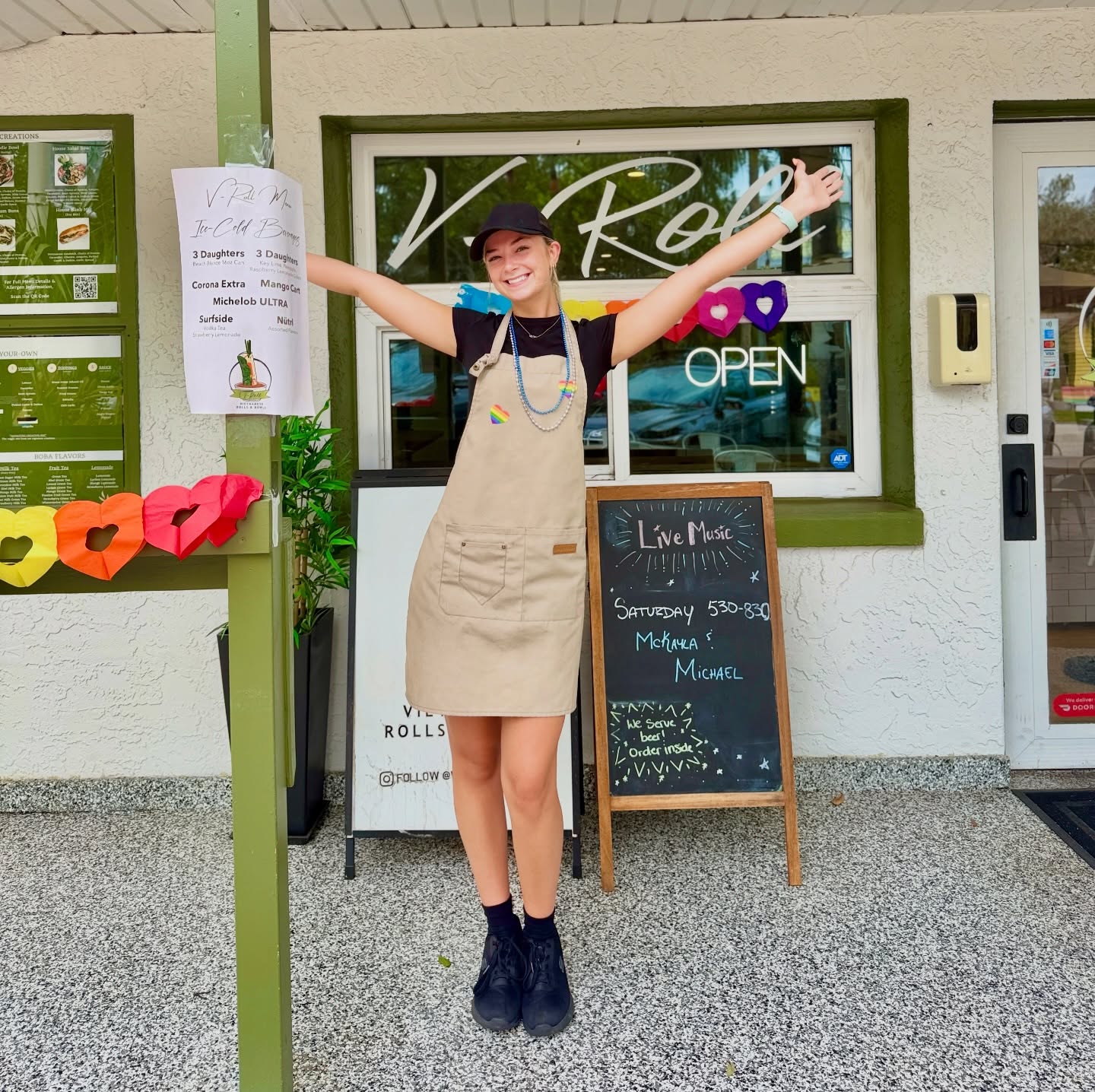 A V-Roll team member with arms wide at the Beach Blvd S door, the Live Music Tonight chalkboard beside her