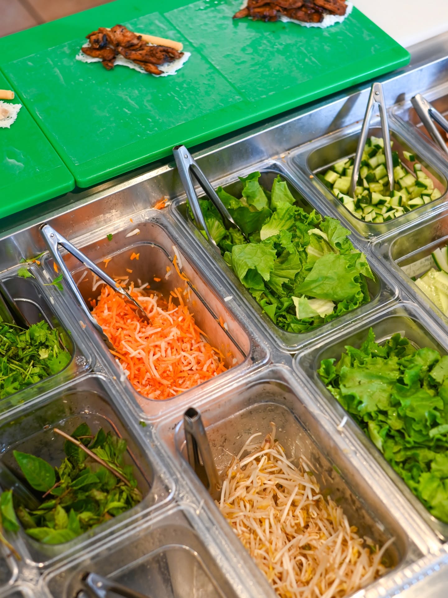 Overhead view of the stainless prep wells on the V-Roll line: lettuce, pickled carrot and daikon, cucumber, bean sprouts and herbs
