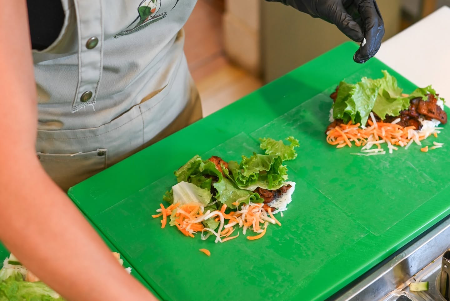 A V-Roll cook building two orders side by side on the green cutting board