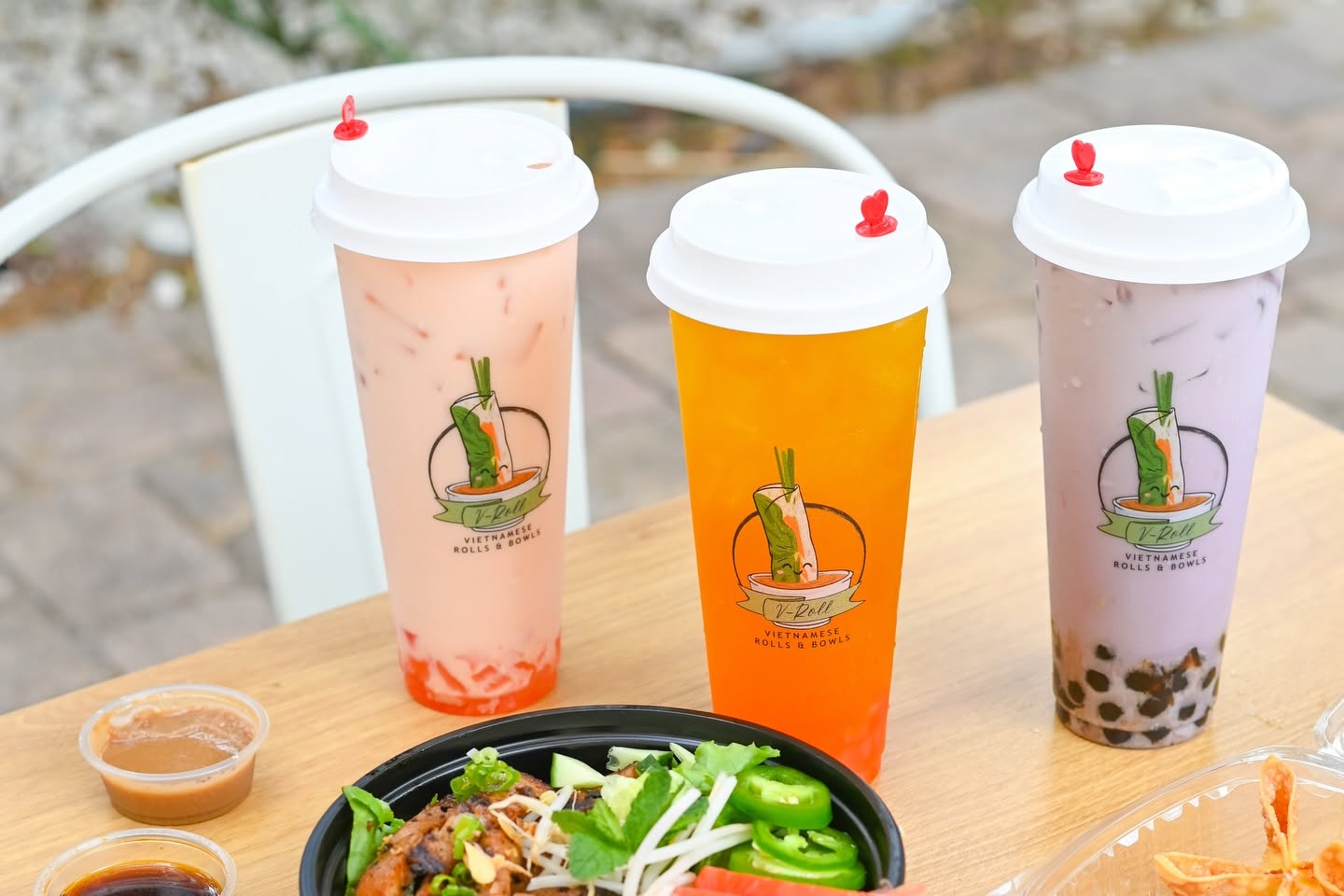 Three boba drinks on a patio table next to a bowl