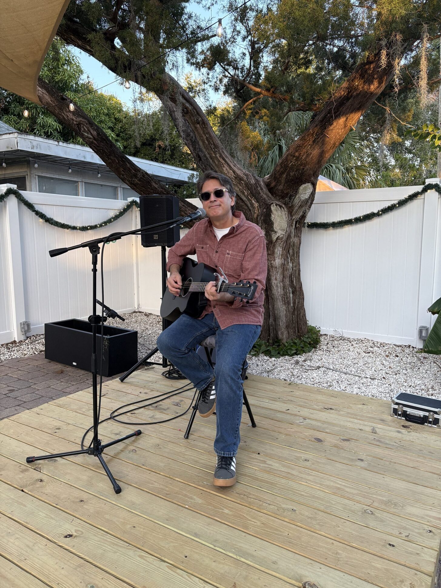 A solo guitarist singing on the wooden patio stage