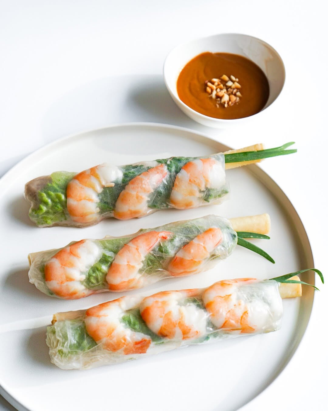 Three Gỏi Cuốn shrimp spring rolls on a white plate with a bowl of peanut sauce
