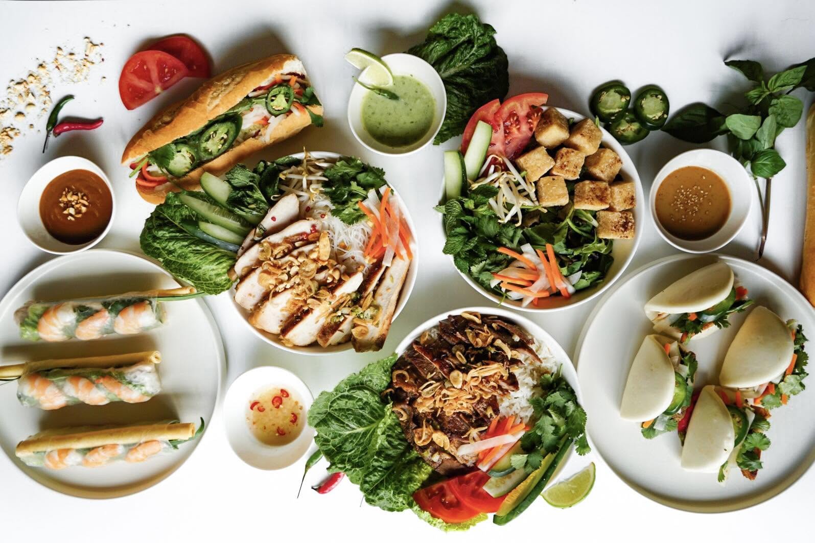 Overhead flat-lay of the full V-Roll menu: bánh mì, bowls, bao, spring rolls and sauces