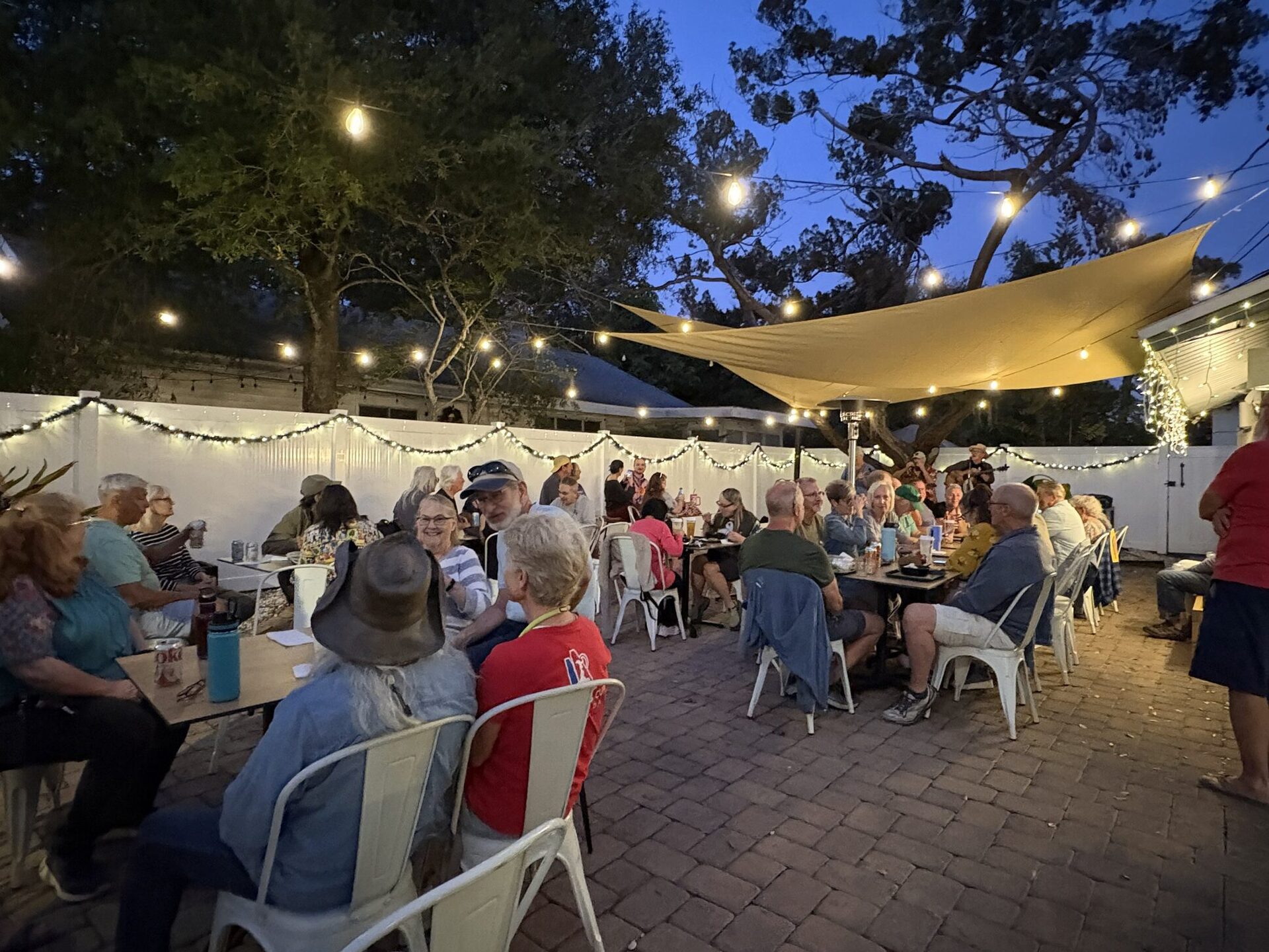The V-Roll patio at dusk under string lights and the shade sail, every table full