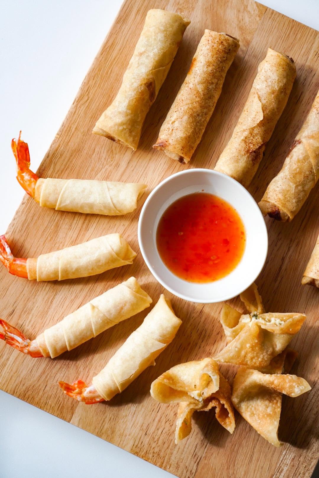 Shrimp rocket rolls and crab wontons on a wood board with sweet chili sauce