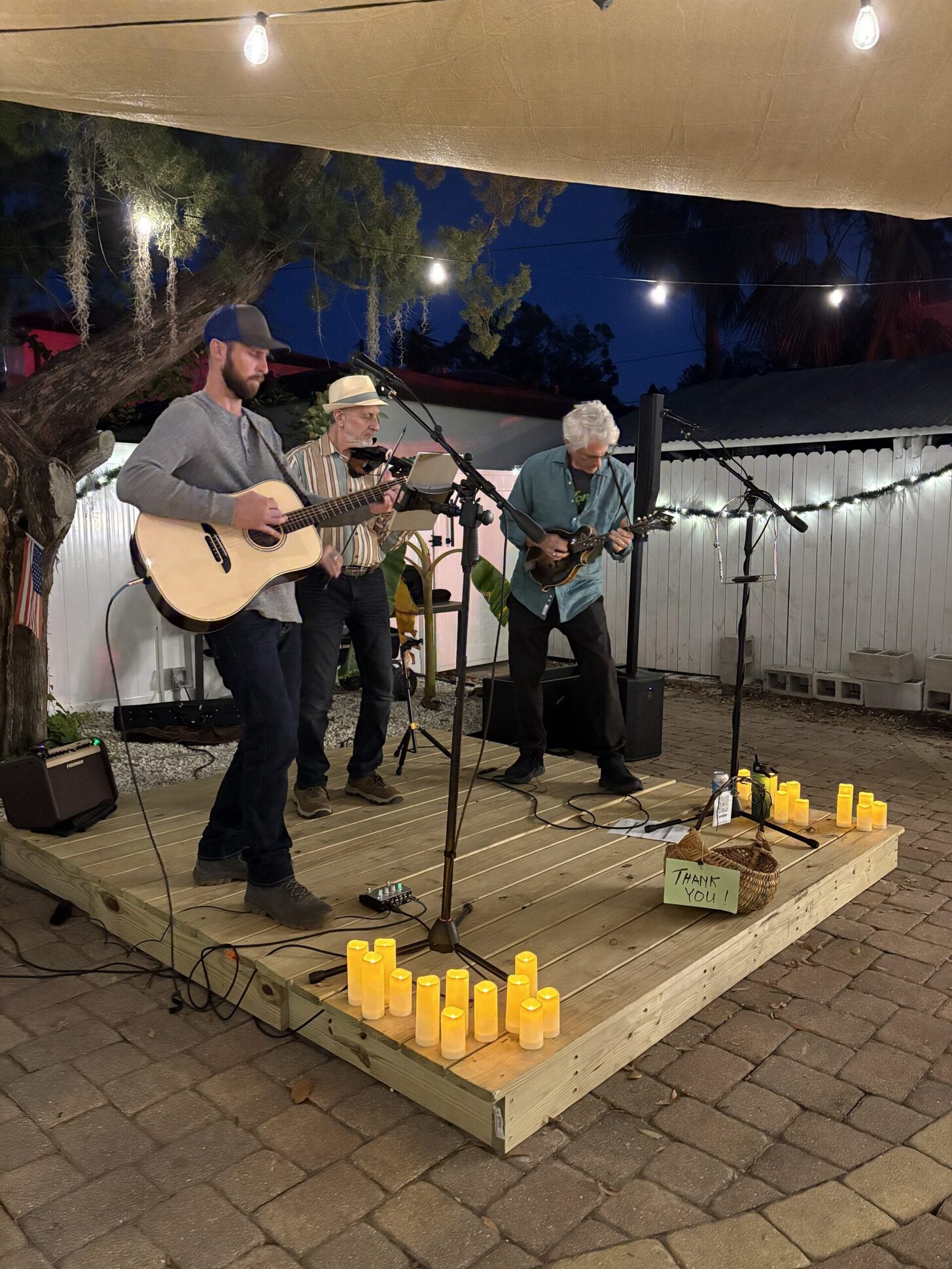Three local musicians playing on the wooden patio stage between candle lanterns