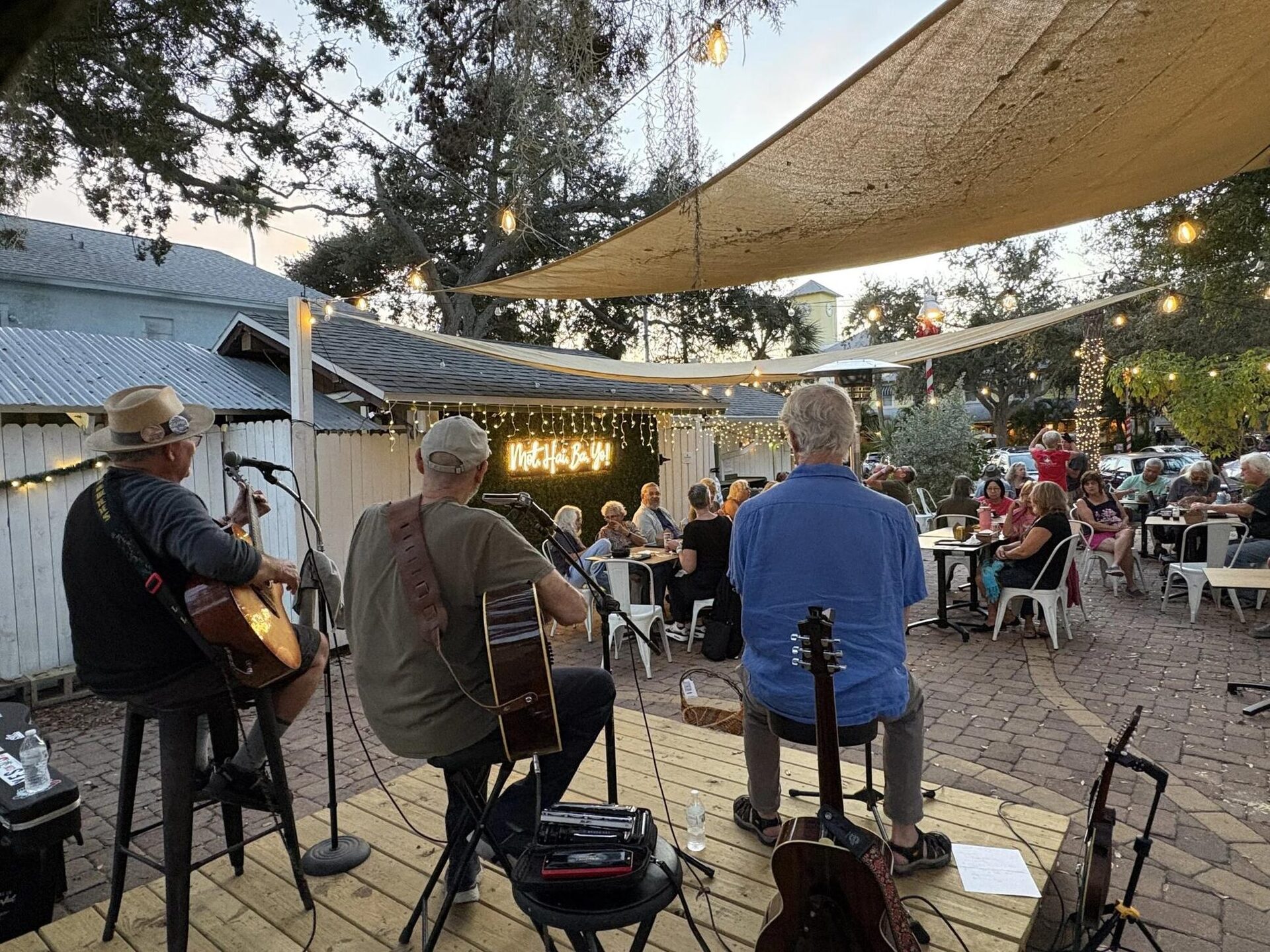 Musicians playing to a full patio under the shade sail